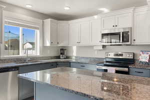 Kitchen with dark stone counters, stainless steel appliances, white cabinetry, and gray cabinets