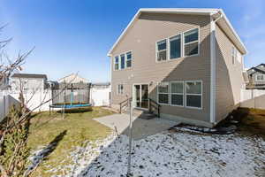 Snow covered back of property with a patio area, a fenced backyard, and a trampoline