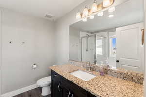 Primary suite full bath with a shower stall, vanity, and dark wood finished floors