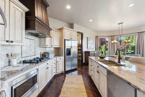 Kitchen featuring cream cabinets, decorative light fixtures, light stone counters, appliances with stainless steel finishes, and dark wood-style floors