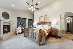 Bedroom featuring high vaulted ceiling, a high end fireplace, light colored carpet, recessed lighting, and a ceiling fan