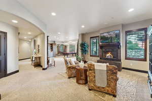 Carpeted living room featuring pool table, arched walkways, recessed lighting, and a warm lit fireplace