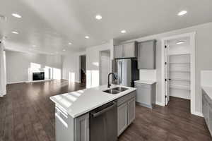 Kitchen with gray cabinets, appliances with stainless steel finishes, a kitchen island with sink, recessed lighting, and a fireplace