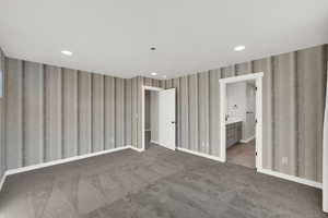 Unfurnished bedroom with recessed lighting, dark colored carpet, wallpapered walls, and ensuite bath