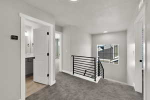 Corridor featuring an upstairs landing, light colored carpet, and a textured ceiling