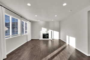 Unfurnished living room with a glass covered fireplace, healthy amount of natural light, dark wood-type flooring, and recessed lighting