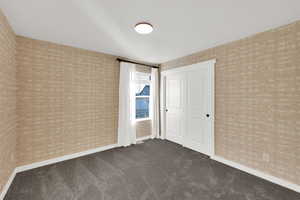 Unfurnished bedroom with dark carpet, brick wall, and wallpapered walls