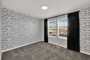 Empty room featuring wallpapered walls and dark carpet