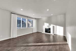Unfurnished living room with a glass covered fireplace, recessed lighting, dark wood-type flooring, and a textured ceiling