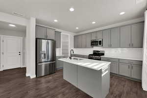 Kitchen with stainless steel appliances, gray cabinets, an island with sink, dark wood finished floors, and decorative backsplash
