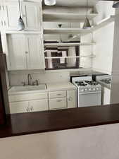 Kitchen with white gas range, white cabinets, and hanging light fixtures