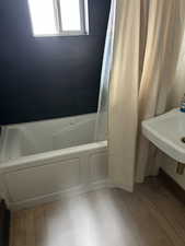 Full bath with a combined bath / shower with jetted tub and light wood-type flooring