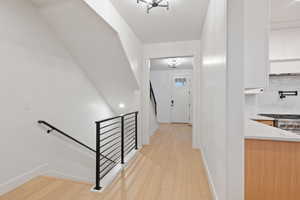 Hallway with light wood-type flooring, an upstairs landing, a chandelier, and a textured ceiling