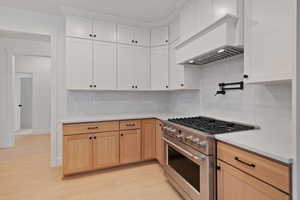 Kitchen featuring high end stainless steel range, light wood-style floors, light stone countertops, and white cabinetry