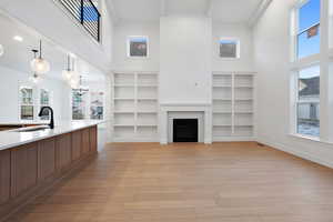 Living area with a towering ceiling, light wood-style floors, a fireplace, and built in shelves