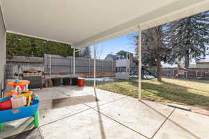 Fenced backyard featuring a playground, a patio area, and a grill