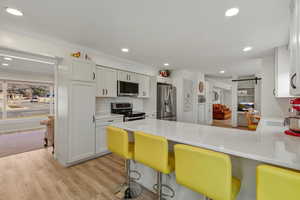 Kitchen featuring a barn door, appliances with stainless steel finishes, a kitchen breakfast bar, a peninsula, and light stone counters