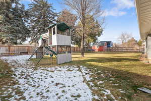 Yard layered in snow featuring a playground, a fenced backyard, and a storage unit