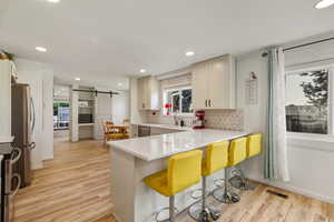 Kitchen with a barn door, a kitchen breakfast bar, a peninsula, light wood-type flooring, and decorative backsplash