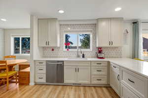 Kitchen with backsplash, light stone counters, dishwasher, light wood-type flooring, and cream cabinetry
