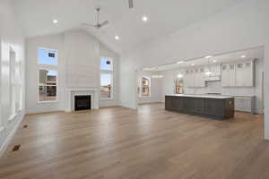 Unfurnished living room with ceiling fan, high vaulted ceiling, a tile fireplace, light wood-style floors, and recessed lighting