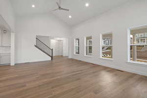 Unfurnished living room featuring a ceiling fan, stairs, wood finished floors, high vaulted ceiling, and recessed lighting