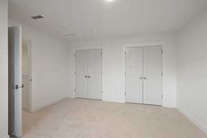 Unfurnished bedroom with multiple closets, light carpet, and attic access
