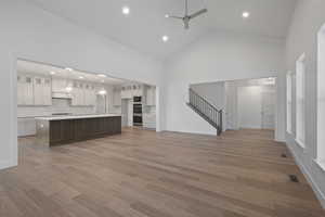 Kitchen featuring light countertops, white cabinets, glass insert cabinets, a large island with sink, and recessed lighting