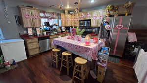 Kitchen with dark countertops, stainless steel appliances, hanging light fixtures, dark wood finished floors, and a kitchen bar