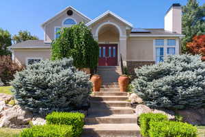 View of front of home featuring solar panels, stucco siding, a chimney, and roof with shingles