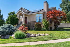 View of front facade with roof mounted solar panels, brick siding, stucco siding, and a chimney