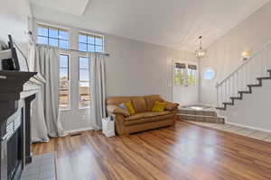 Living area featuring vaulted ceiling, stairway, light wood finished floors, a fireplace with flush hearth, and a chandelier