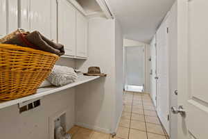 Laundry area with cabinet space, light tile patterned flooring, and lofted ceiling