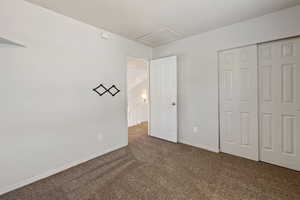 Unfurnished bedroom with dark colored carpet, attic access, and a closet
