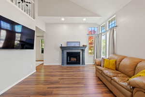 Living area with a tile fireplace, wood finished floors, high vaulted ceiling, recessed lighting, and healthy amount of natural light