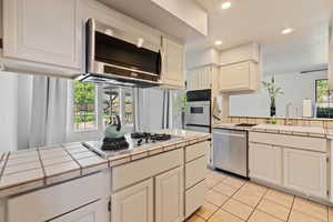 Kitchen featuring tile counters, stainless steel appliances, light tile patterned floors, recessed lighting, and white cabinetry