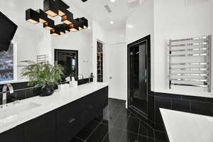 Full bathroom with a towel warming rack, radiator, double vanity, dark tile patterned flooring, and a tub