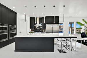 Kitchen with dark cabinetry, hanging light fixtures, a breakfast bar area, and recessed lighting