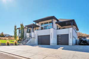 Contemporary home featuring a balcony, driveway, stucco siding, an attached garage, and stairs