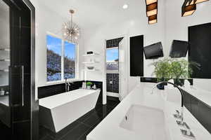 Bathroom with double vanity, a freestanding tub, dark tile patterned flooring, and tile walls