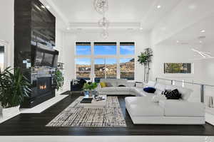 Living room featuring dark wood-style flooring, a fireplace, recessed lighting, a high ceiling, and a chandelier