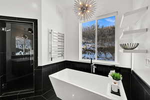 Bathroom with radiator heating unit, a towel warmer, a soaking tub, a stall shower, and a chandelier