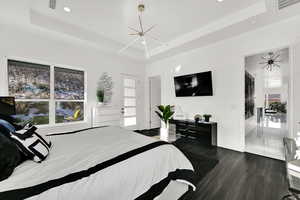 Bedroom featuring a raised ceiling, dark wood-style floors, multiple windows, and recessed lighting