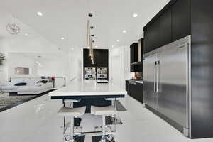 Kitchen with dark cabinetry, hanging light fixtures, a kitchen bar, recessed lighting, and appliances with stainless steel finishes