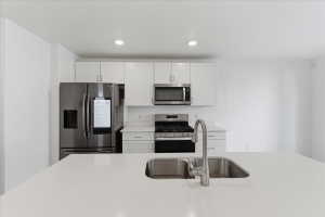 Kitchen featuring appliances with stainless steel finishes, white cabinetry, recessed lighting, and light stone counters