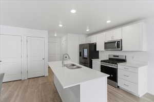 Kitchen with appliances with stainless steel finishes, white cabinets, a kitchen island with sink, light wood-type flooring, and recessed lighting
