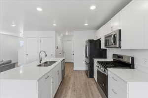 Kitchen with stainless steel appliances, a center island with sink, white cabinets, light wood-style floors, and light stone countertops