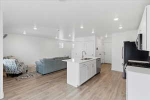 Kitchen with white cabinets, open floor plan, a kitchen island with sink, light wood-style flooring, and recessed lighting