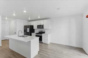 Kitchen featuring stainless steel appliances, white cabinets, a center island with sink, light wood-style floors, and recessed lighting