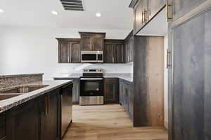 Kitchen featuring appliances with stainless steel finishes, dark brown cabinetry, light stone counters, light wood finished floors, and recessed lighting
